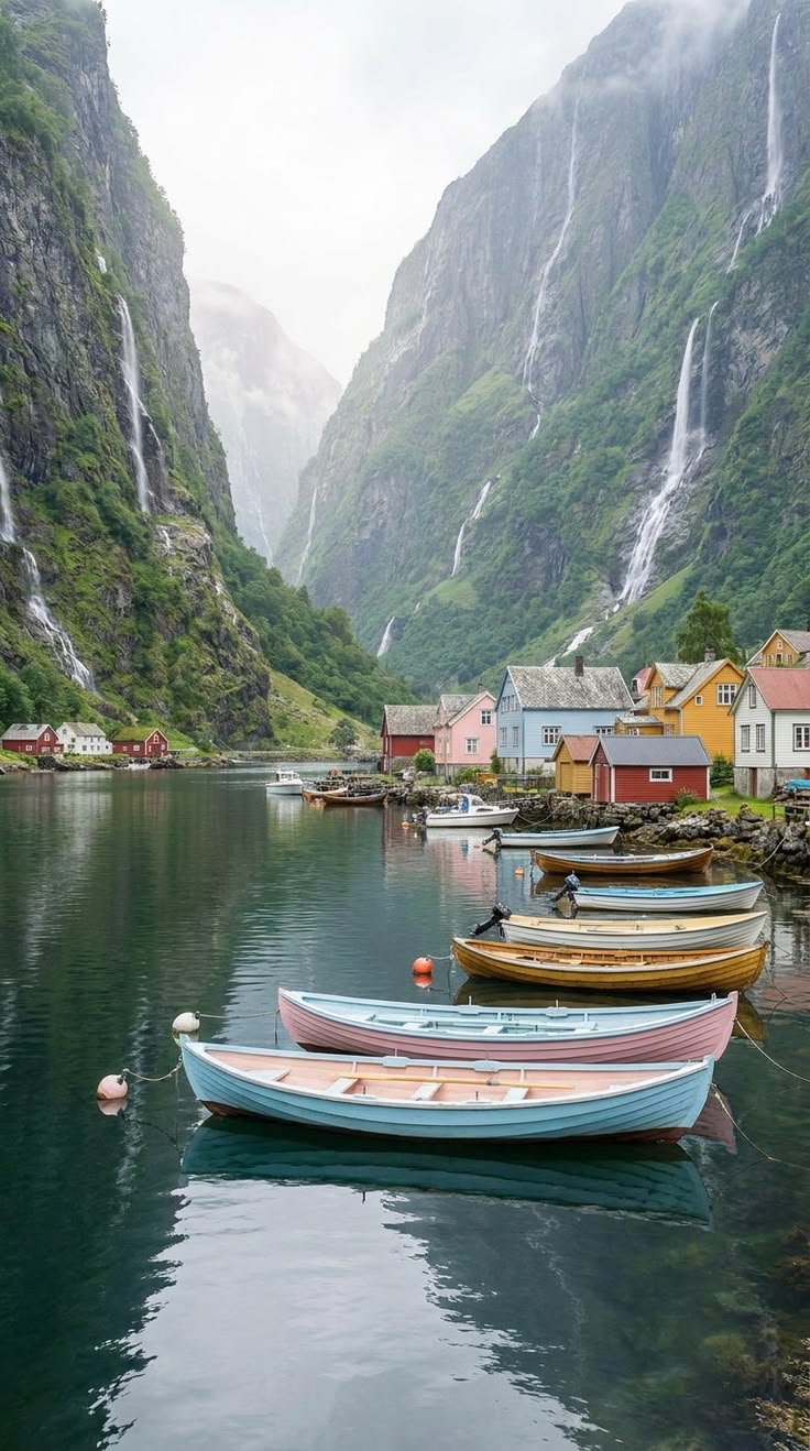 This may contain: several boats are docked in the water near some mountains and houses with waterfalls on them