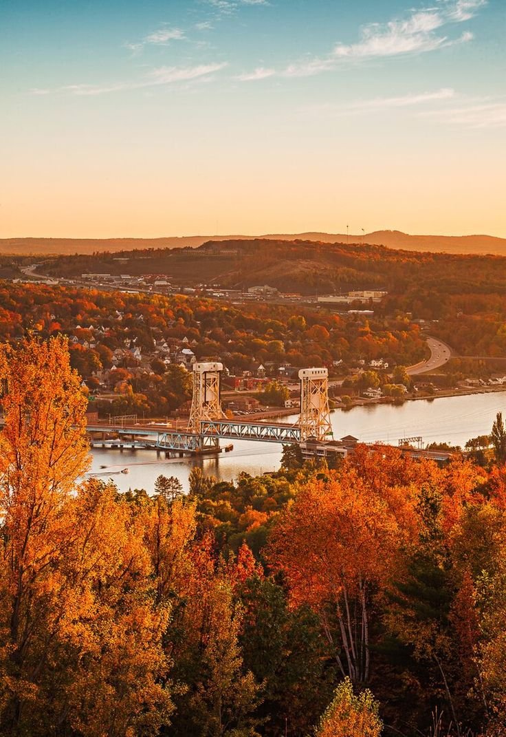 This may contain: an aerial view of a bridge over a river surrounded by autumn foliage and trees in the foreground