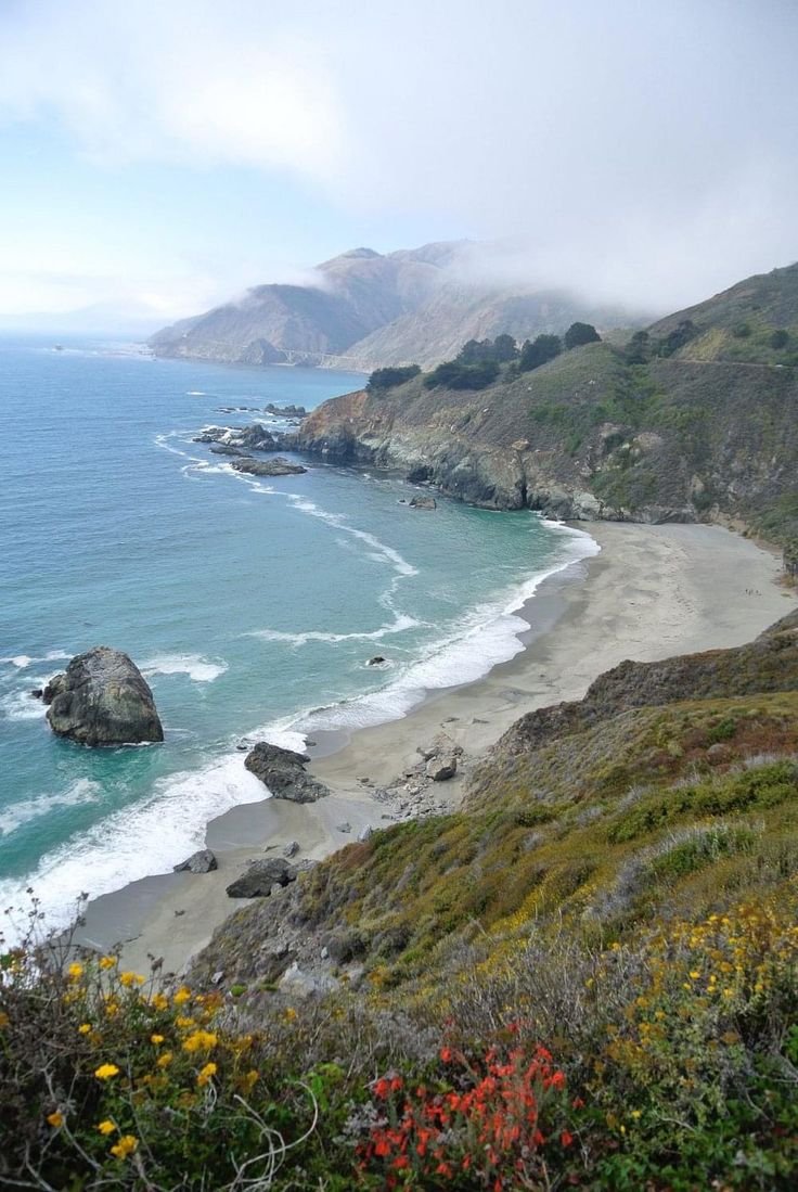 This may contain: the beach is surrounded by rocky cliffs and wildflowers on the side of the water