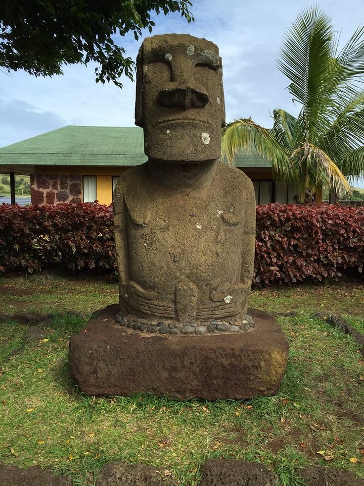 This may contain: a large stone statue sitting on top of a lush green field next to a house