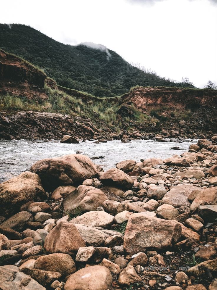 This may contain: rocks and water in the middle of a rocky river bed with mountains in the background