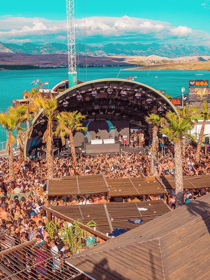 This may contain: an aerial view of a festival with lots of people on the stage and water in the background