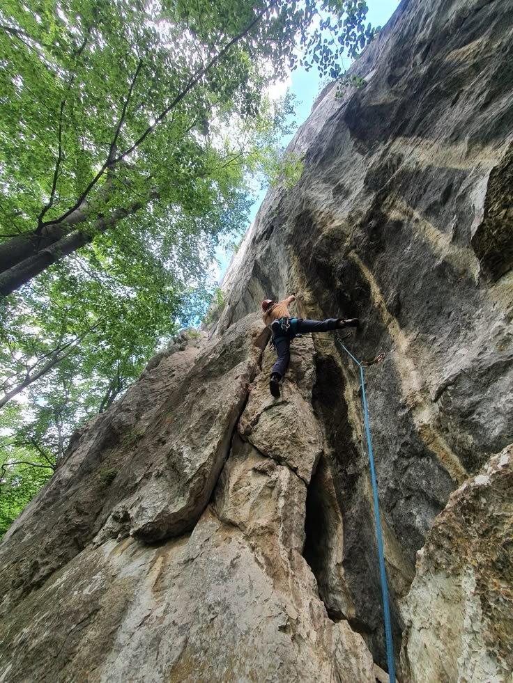 This may contain: a man climbing up the side of a large rock with ropes attached to it's sides