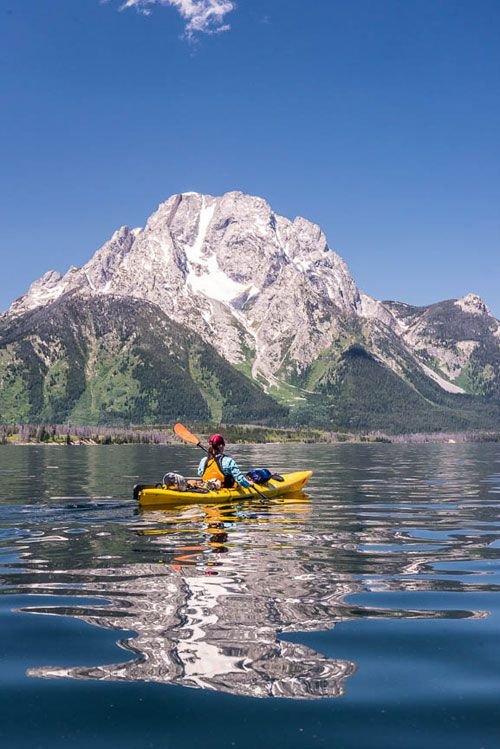This may contain: a person in a kayak paddling on the water with mountains in the background